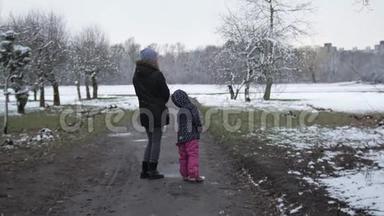 妈妈带着一个女儿在春天多云的公园里散步，下雪了